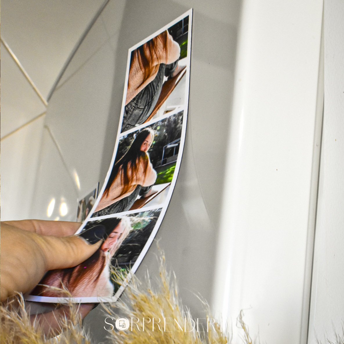 Mano colocando un imán fotomatón clásico personalizado de 6.5x21 cm en la puerta de la nevera, mostrando cómo se utiliza el producto.